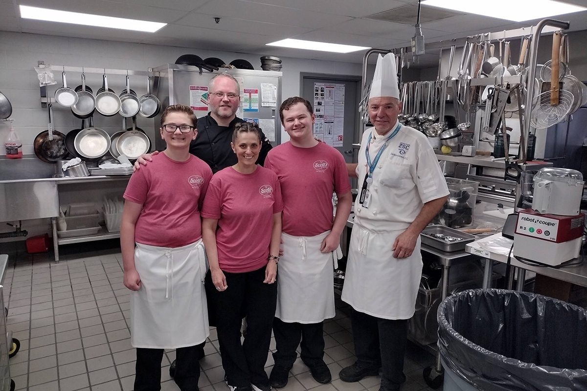 Five people smiling in a kitchen.